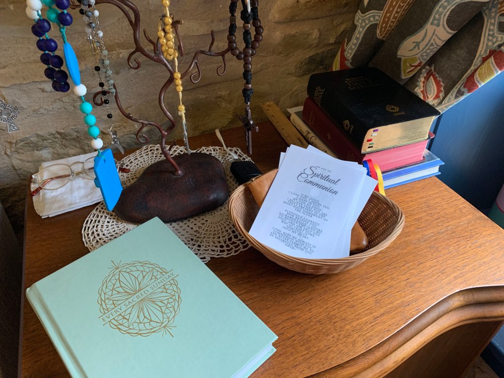 Prayer table with rosaries hanging, Mass journal, spiritual reading, and basket of spiritual communion prayer cards.
